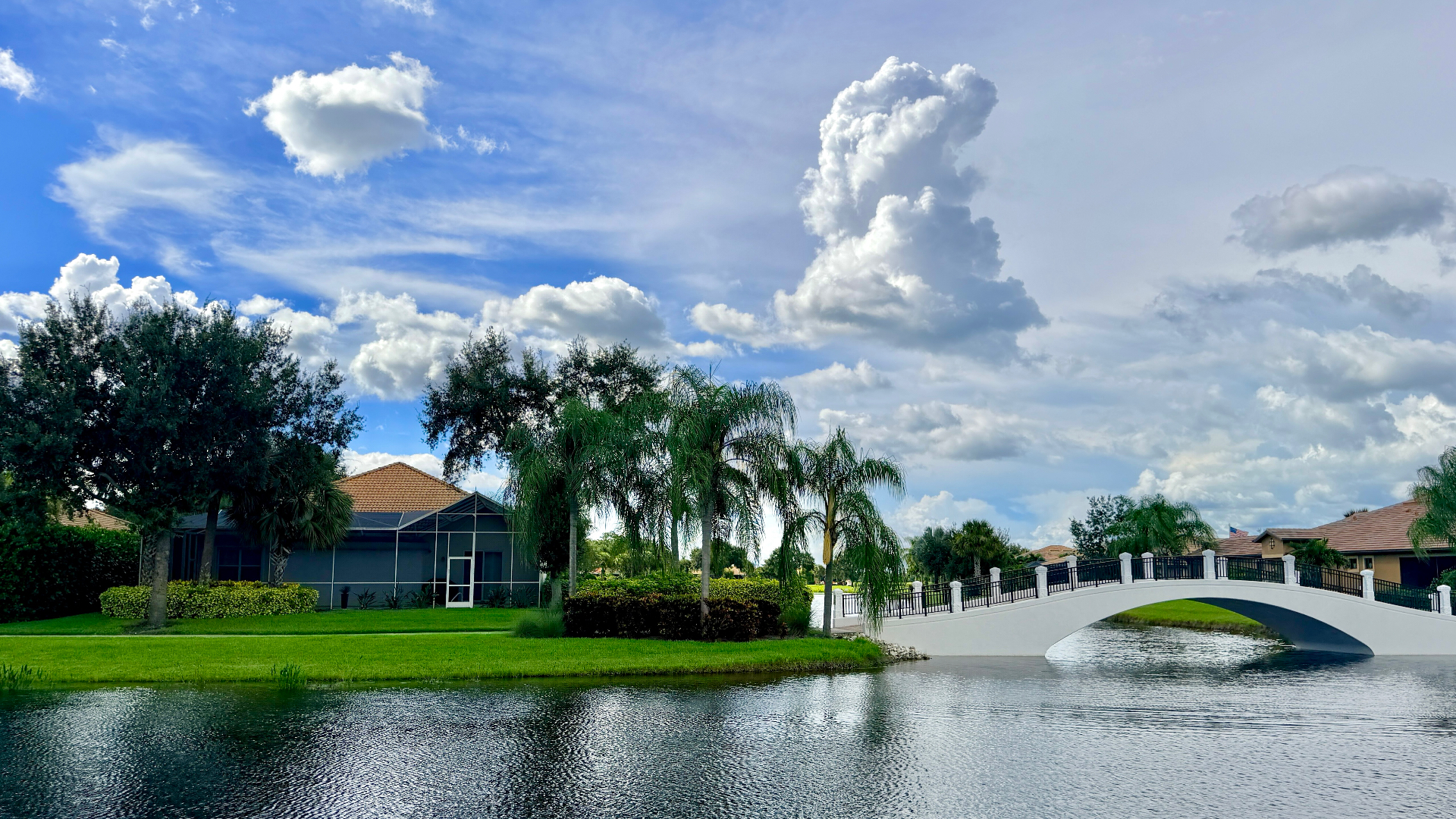 Palm-lined residential street with cream stucco homes and a lake footbridge in the Bellera community of Ave Maria, Florida