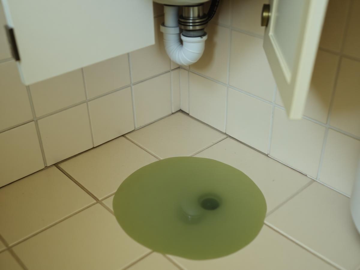 Small pool of water on a tile floor beneath a bathroom sink cabinet